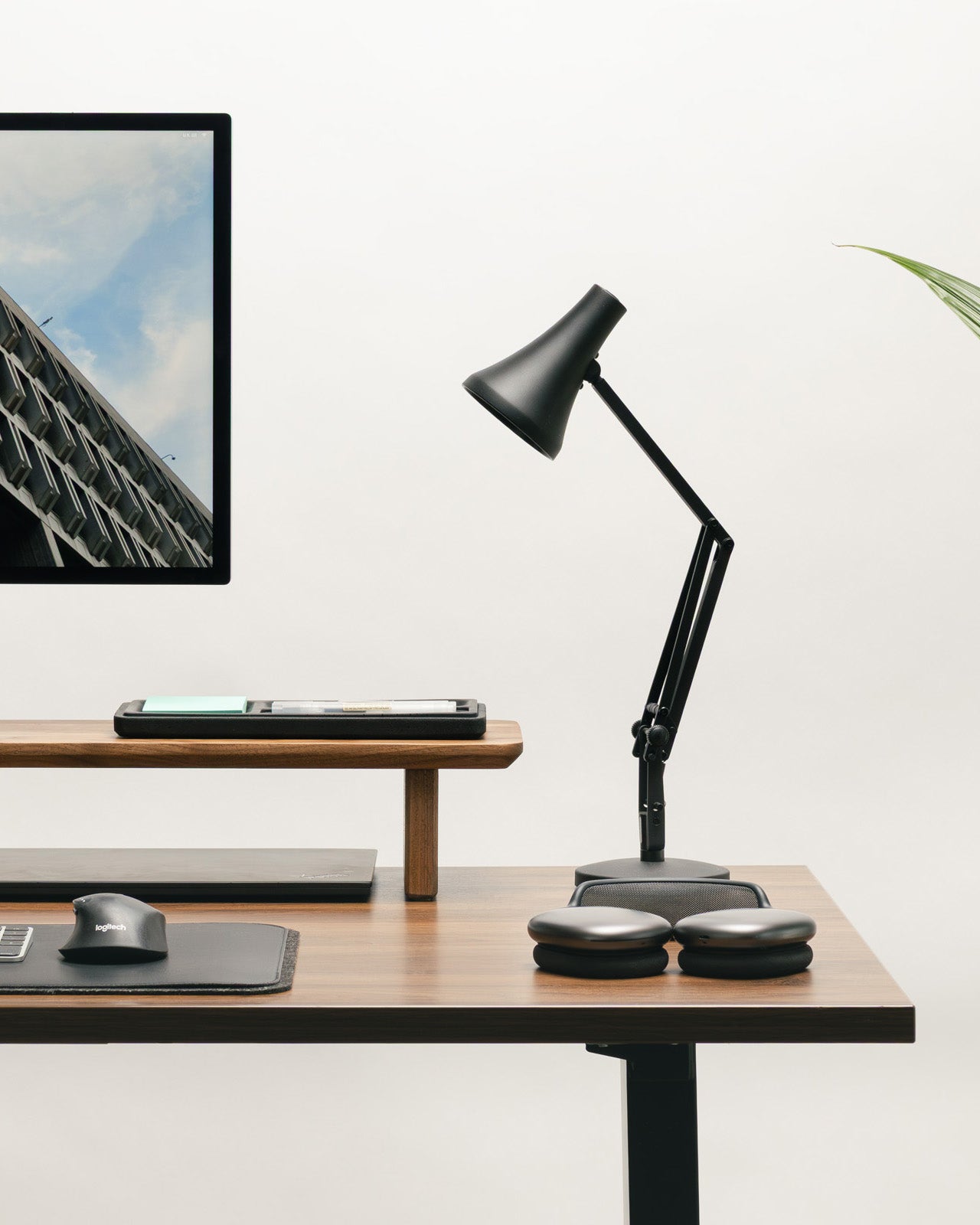 Black adjustable desk lamp on a wooden desk with a computer monitor in the background.