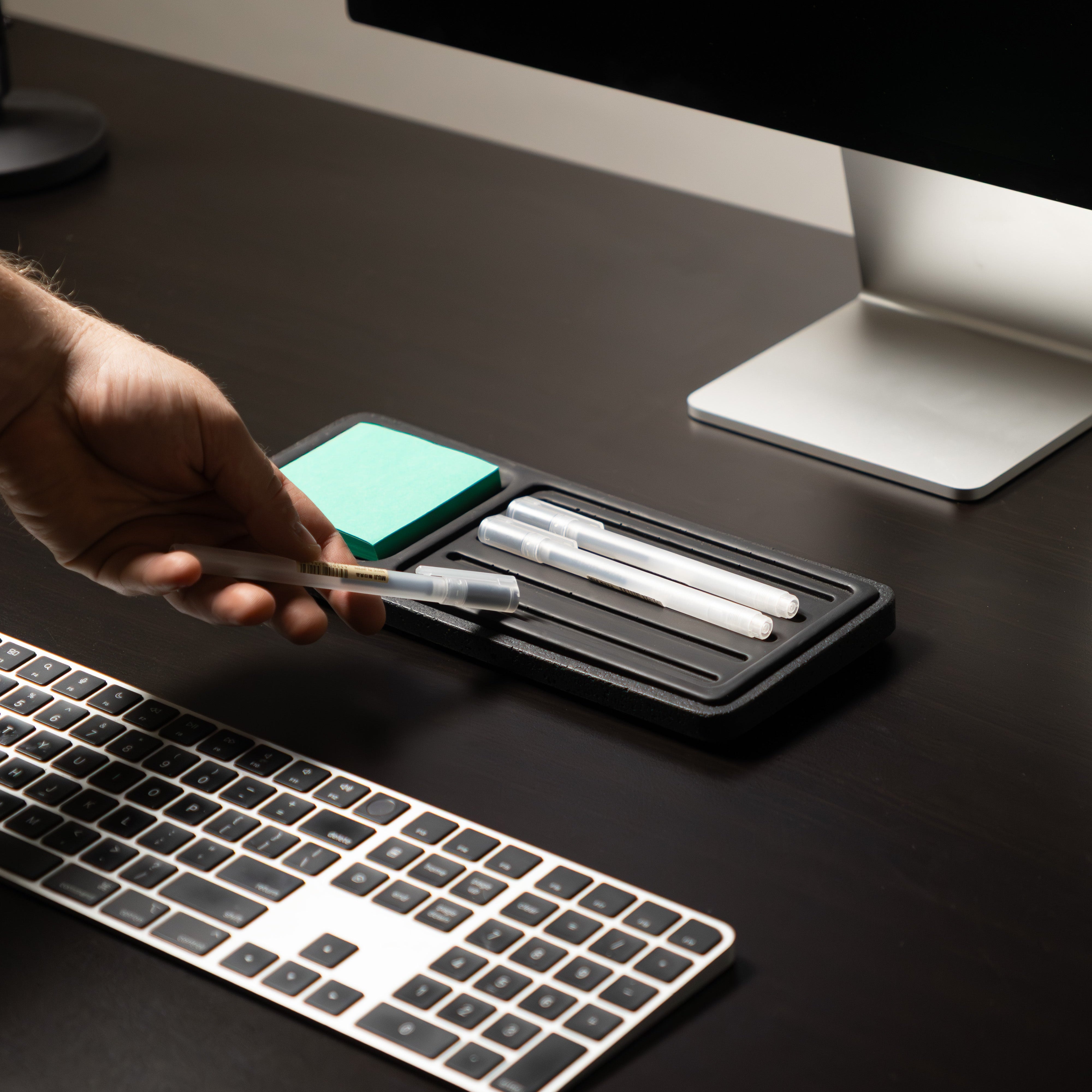 Person using a pen on a desk with a computer and keyboard in the background