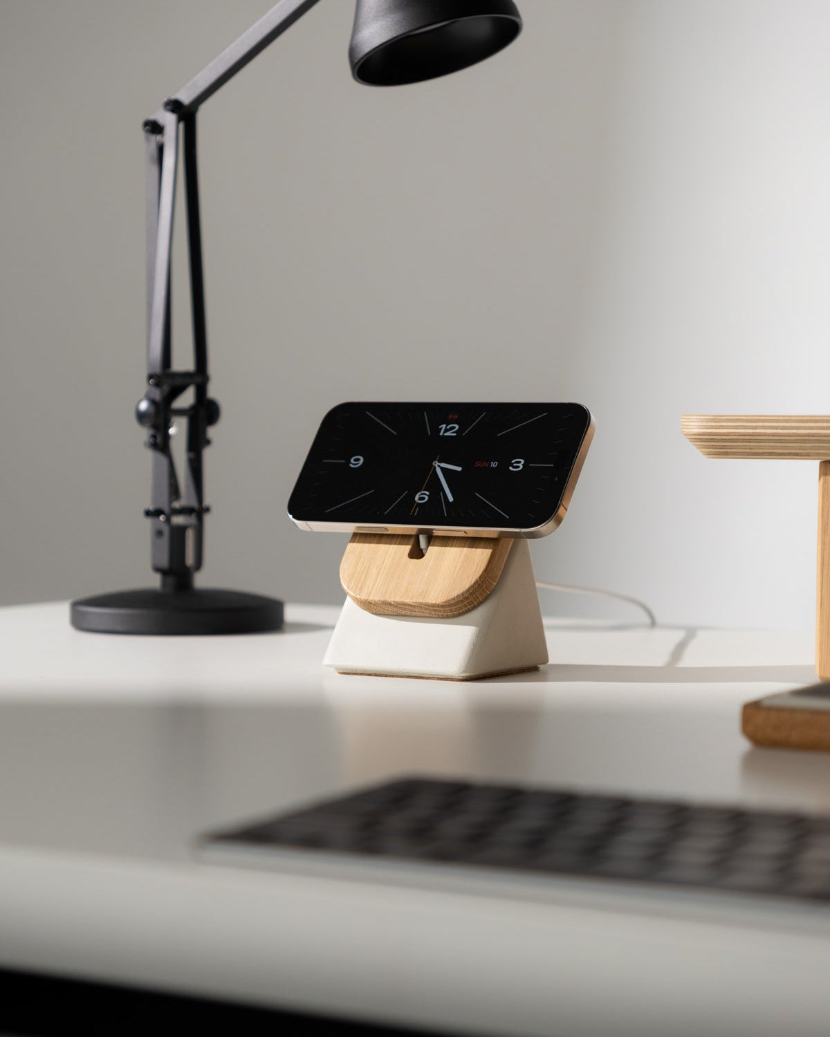 Black lamp and smartphone on a stand on a white desk with a gray wall background