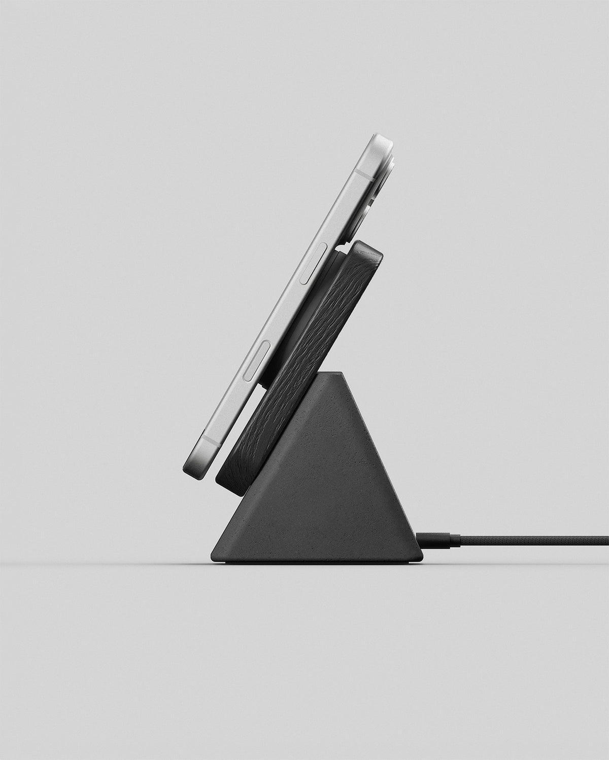 Upright wireless charging stand in black wood and charcoal concrete, side view with a smartphone charging