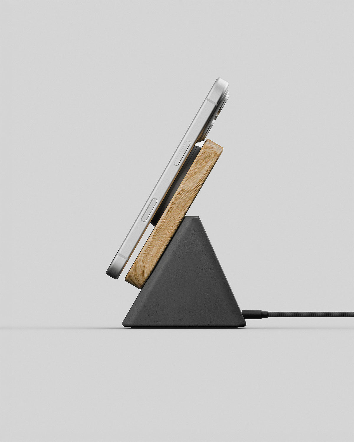 Upright wireless charging stand in oak and charcoal concrete, side view with a smartphone charging