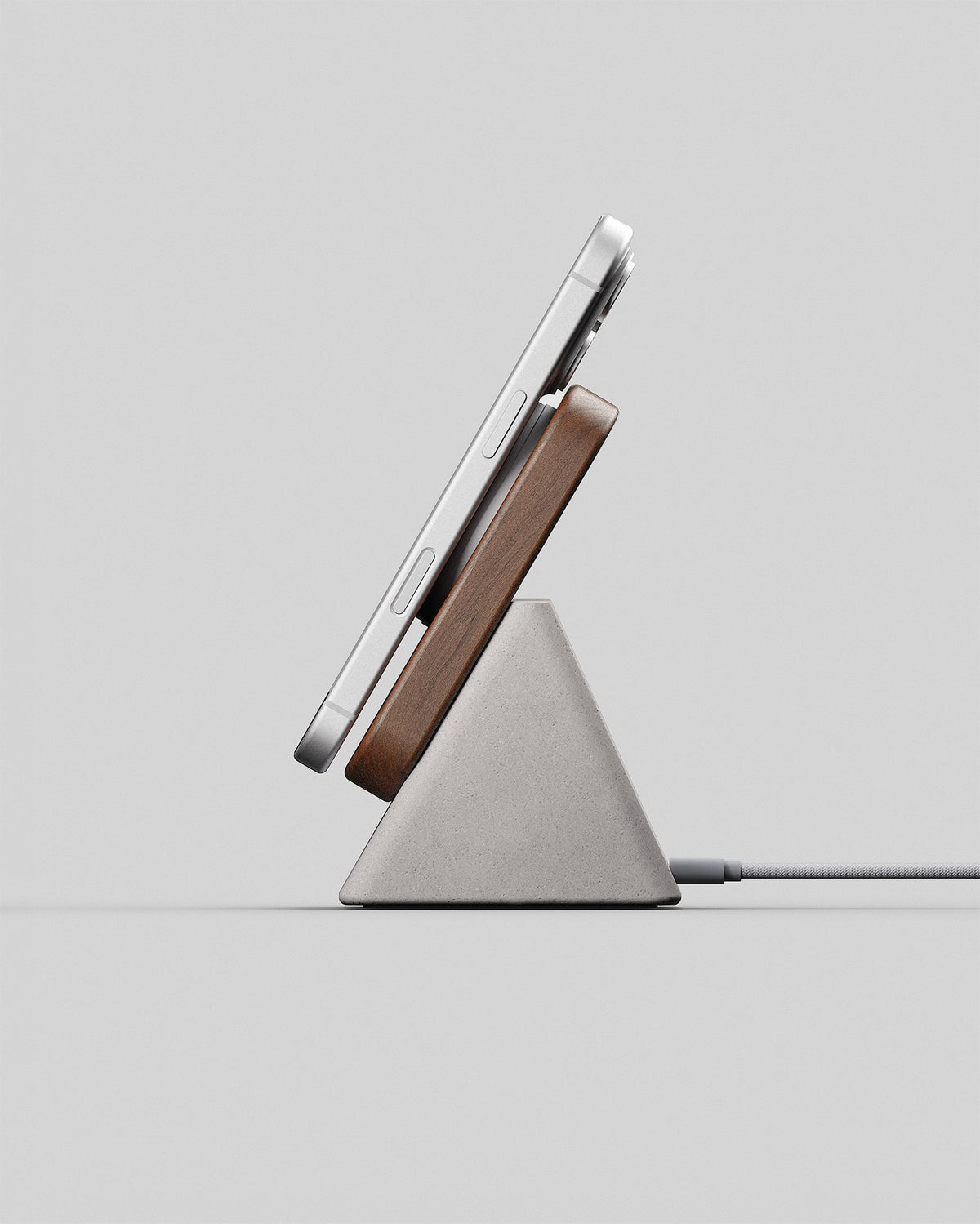 Upright wireless charging stand in walnut and stone concrete, side view with a smartphone charging