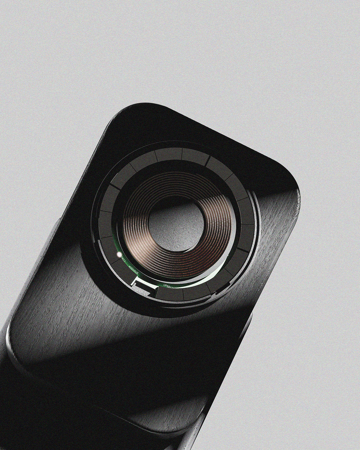 A close-up studio shot of a black rectangular electronic device with a circular metallic component, set against a solid light gray background.