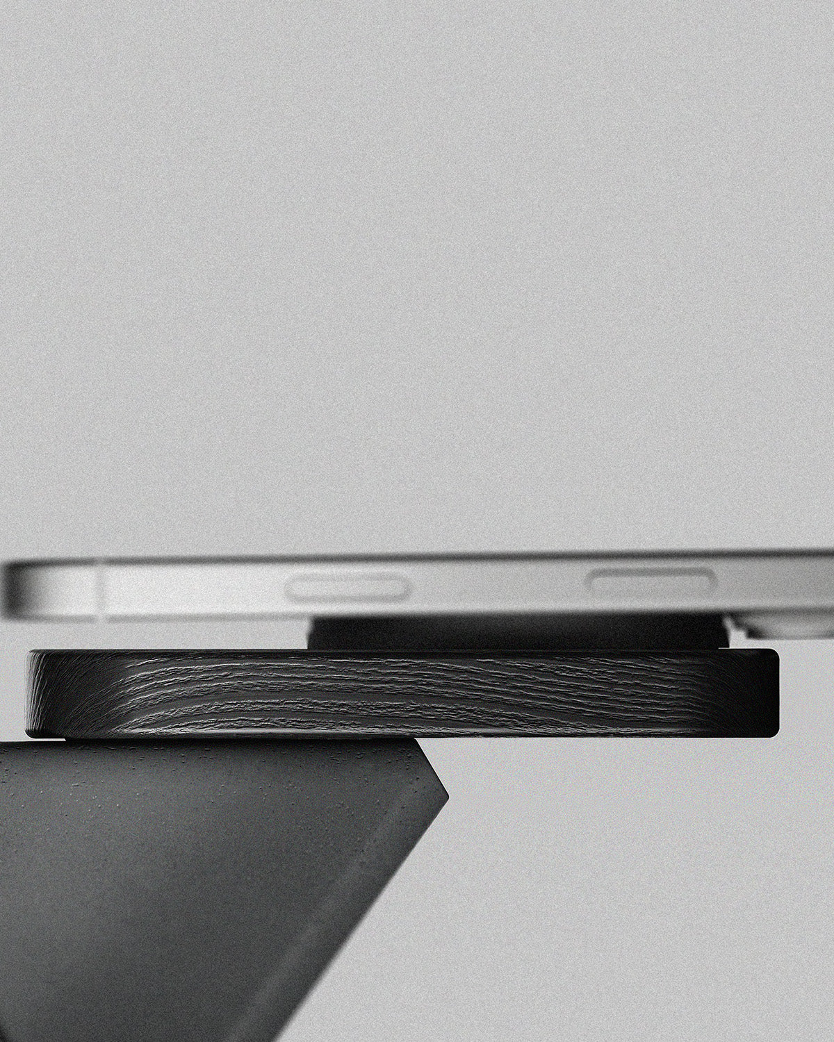 Close-up of a black wireless phone charger from Modhaus, showing the side  a black textured  wood and concrete surface, set against a minimalist light gray background.