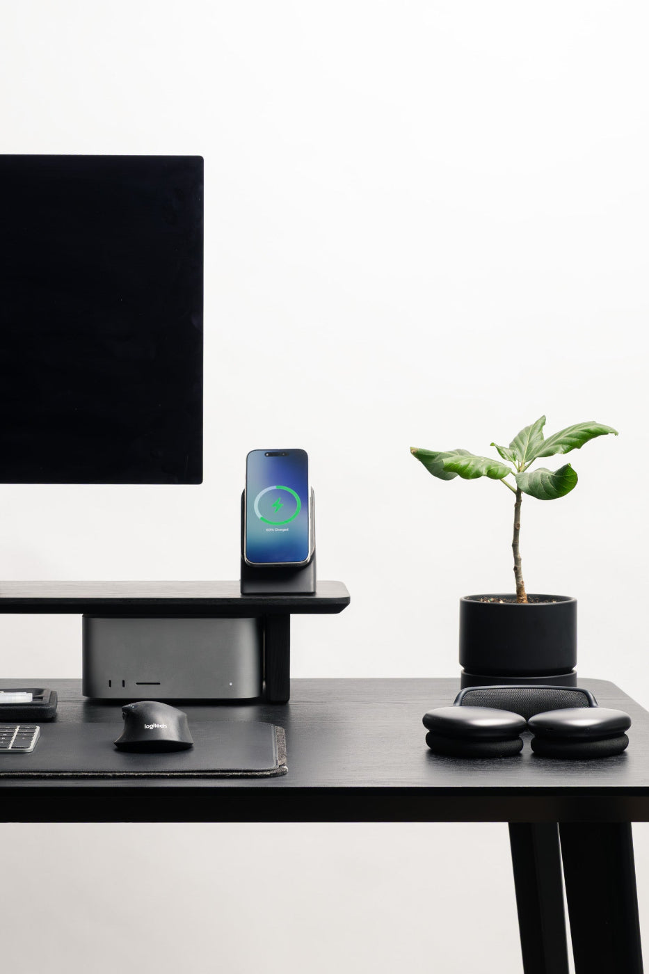 Modern office desk setup with computer monitor, smartphone on wireless charger, and small plant.