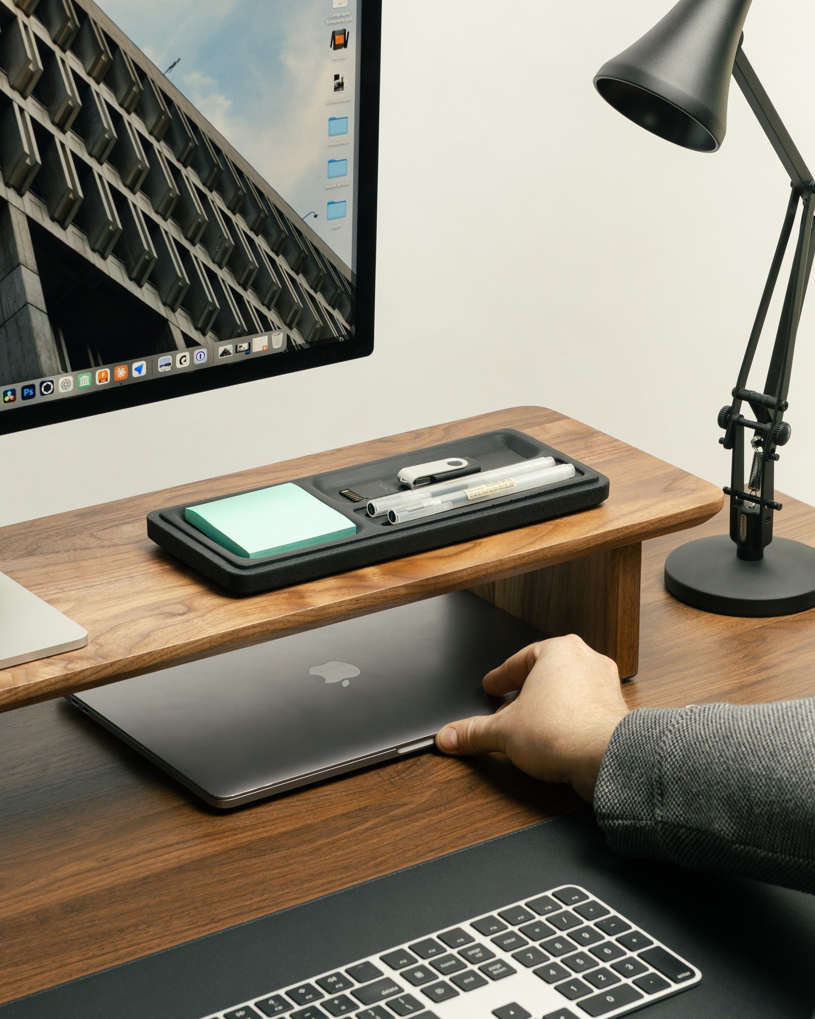 Person using a laptop on a wooden desk with a monitor, phone, and lamp in the background.