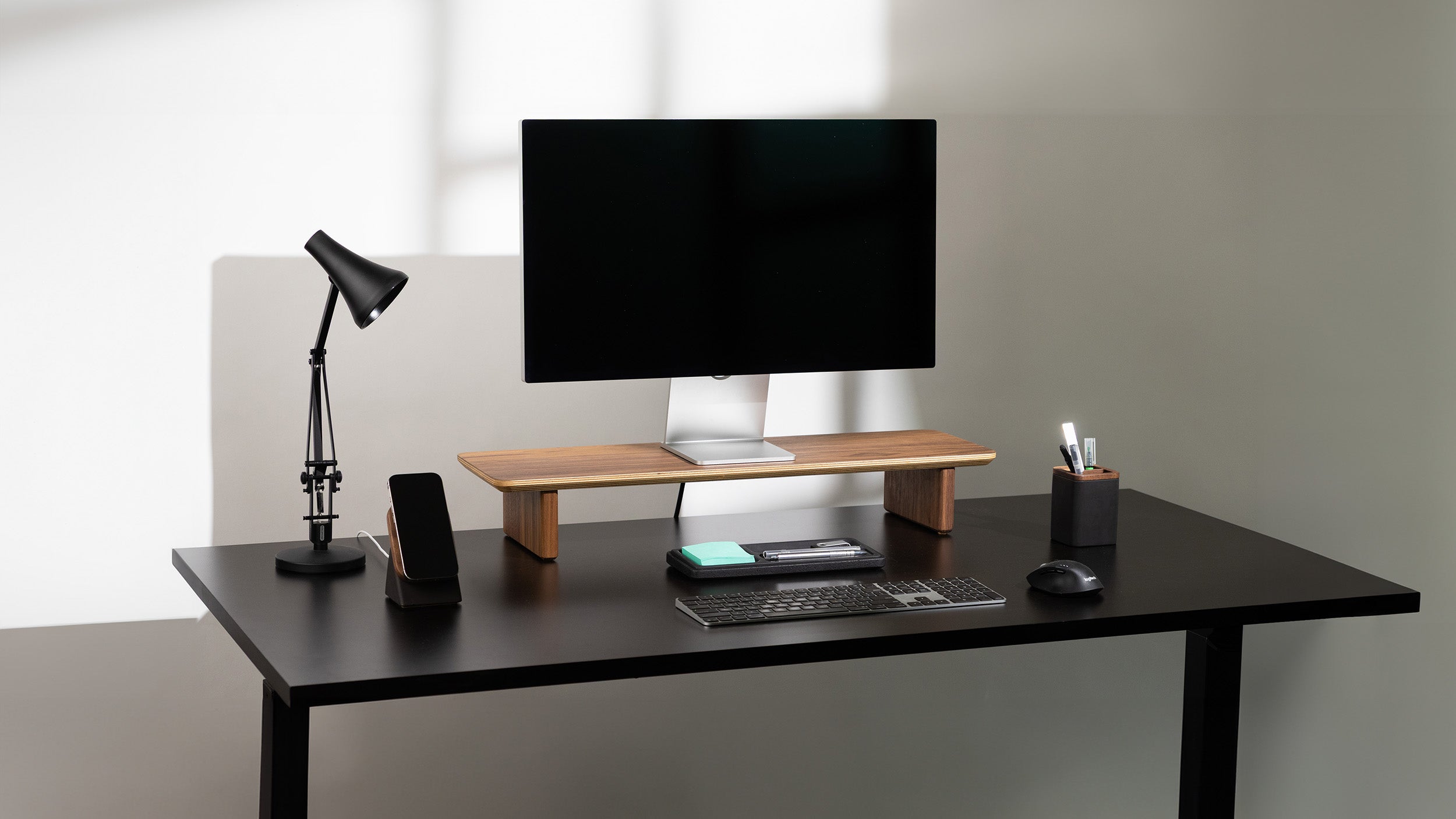 Modern office desk setup with a monitor, lamp, and other items on a plain background