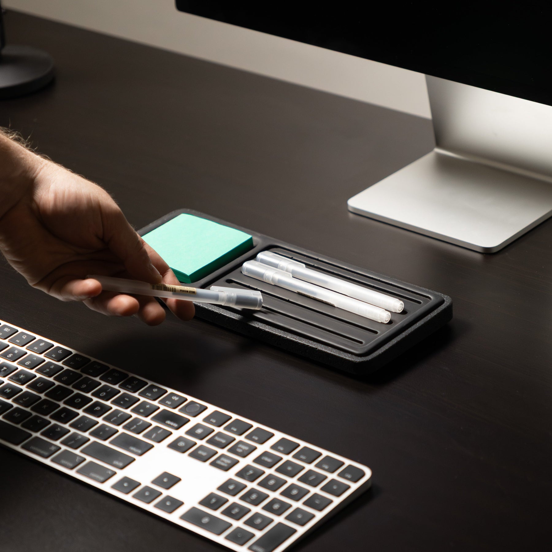 Person using a pen on a desk with a computer and keyboard in the background