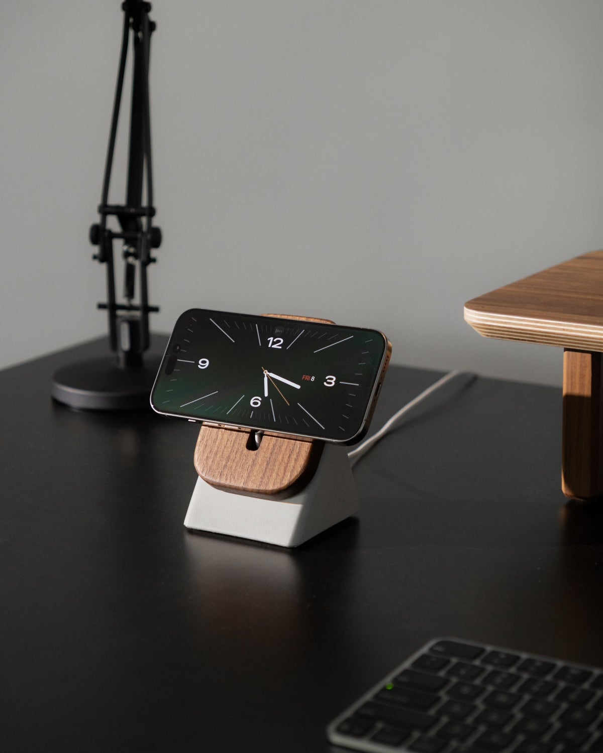 Smartphone on a stand with a clock display on a desk with a lamp and keyboard.